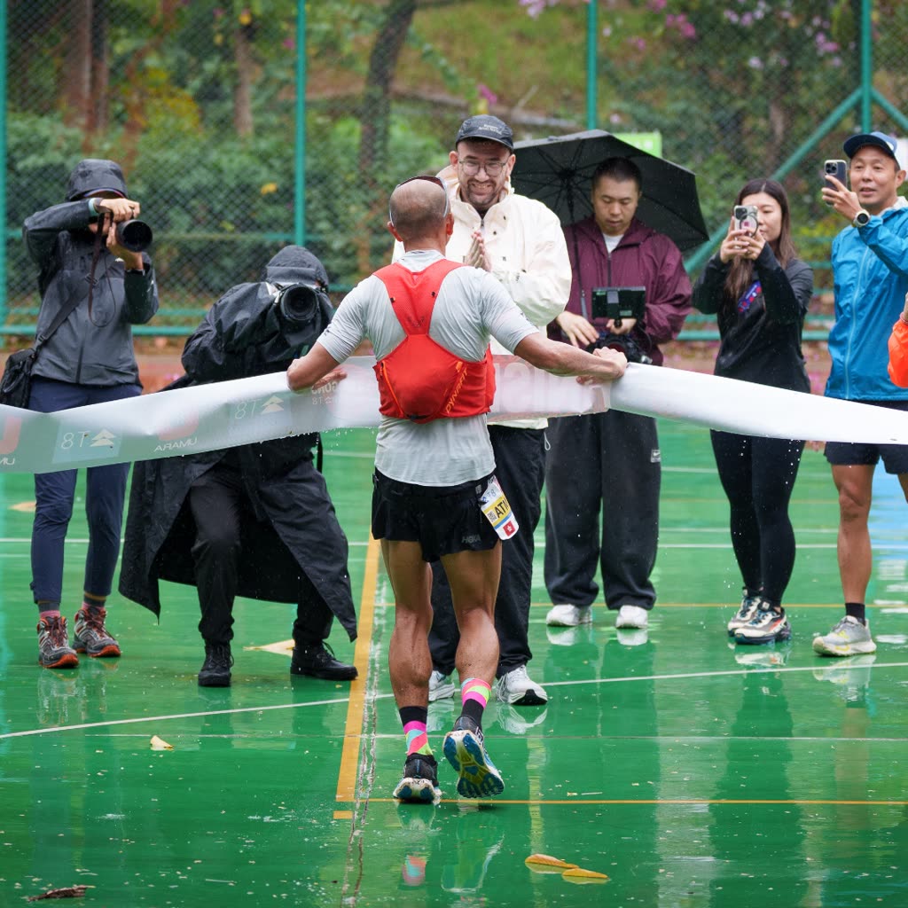 A runner approaches the finish line of the 9 Dragons Ultra in Hong Kong, met by the race director and photographers